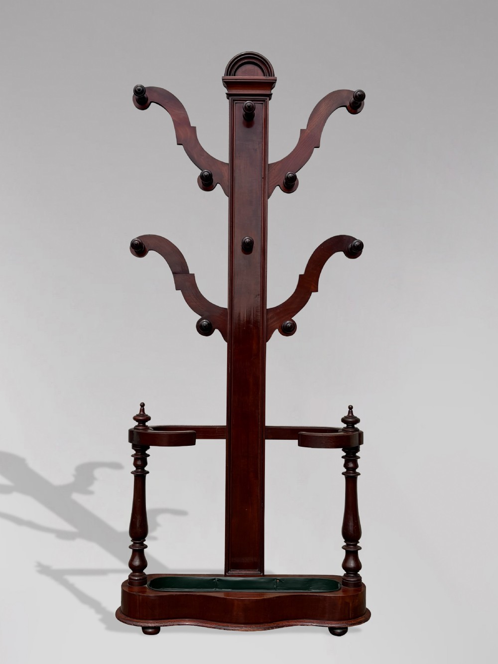 A 19th-century Victorian mahogany hall stand with carved coat pegs, turned supports, and an umbrella base featuring a green drip tray. View IX