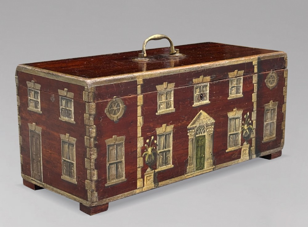A rectangular dark red painted oak box decorated with a detailed Georgian house facade, featuring a brass handle on the top lid.