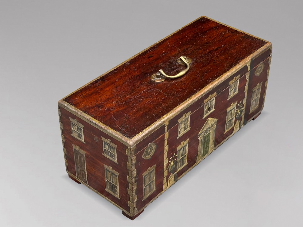 A rectangular dark red painted oak box decorated with a detailed Georgian house facade, featuring a brass handle on the top lid. View V