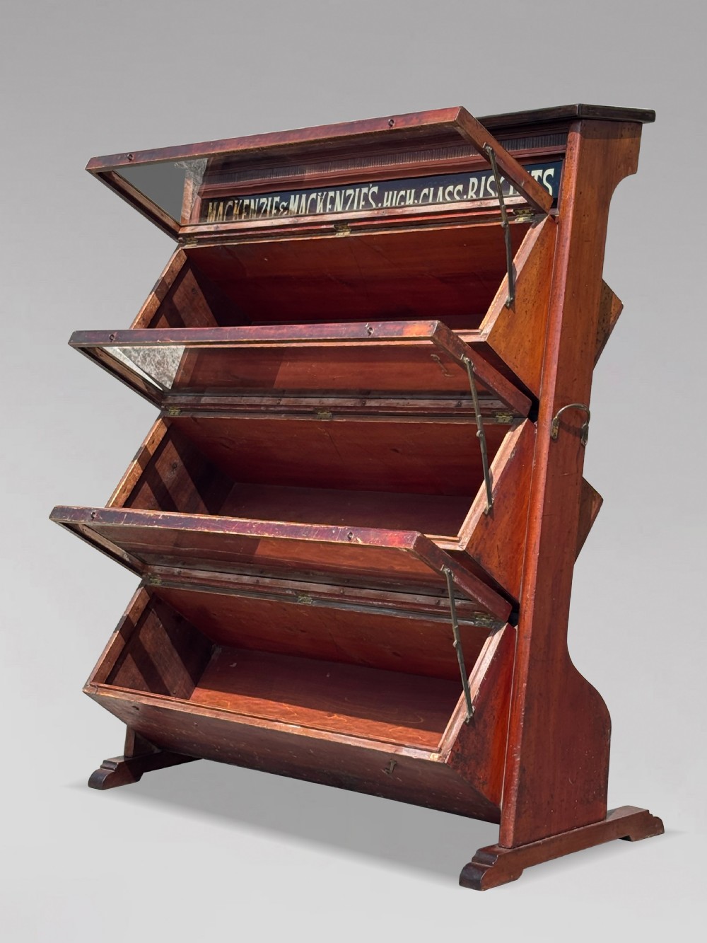 A late 19th-century mahogany three-tiered biscuit display cabinet featuring angled glass fronts, brass handles, and a painted advertising header for Mackenzies Biscuits. View III