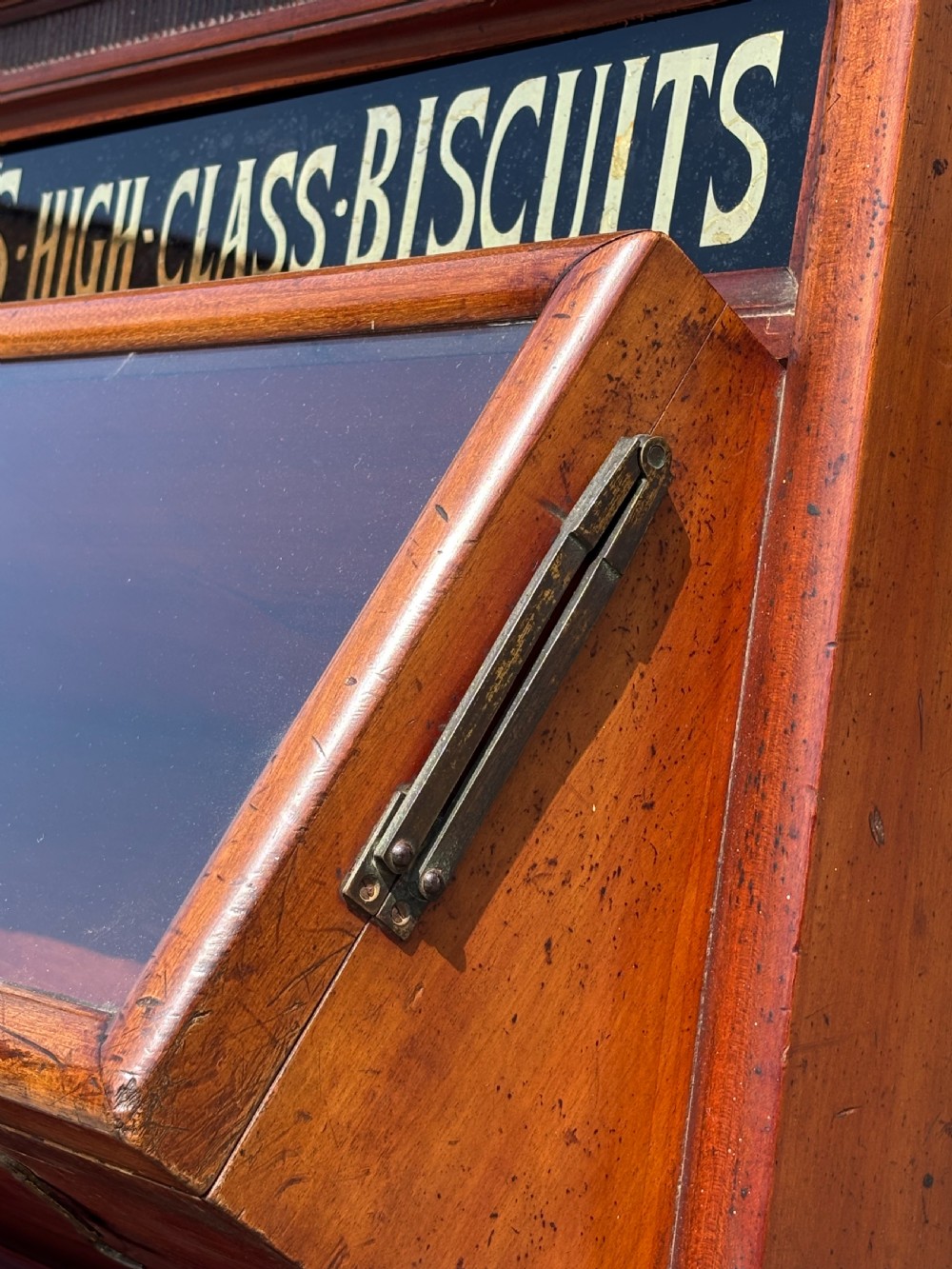 A late 19th-century mahogany three-tiered biscuit display cabinet featuring angled glass fronts, brass handles, and a painted advertising header for Mackenzies Biscuits. View VII