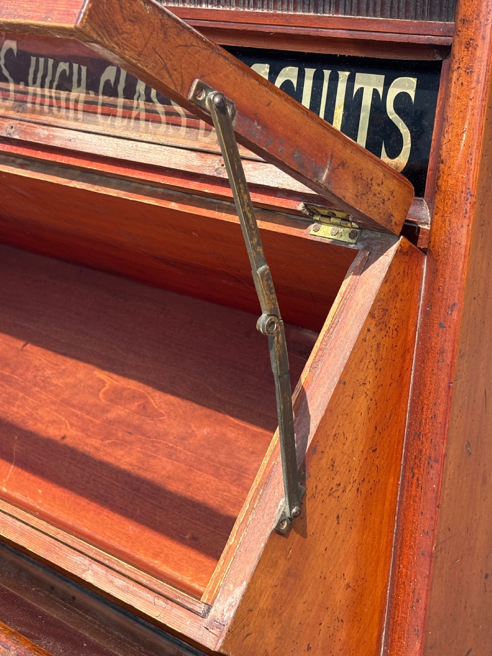A late 19th-century mahogany three-tiered biscuit display cabinet featuring angled glass fronts, brass handles, and a painted advertising header for Mackenzies Biscuits. View VIII