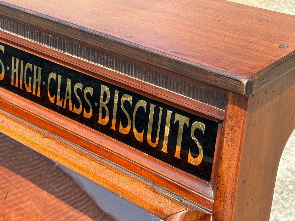A late 19th-century mahogany three-tiered biscuit display cabinet featuring angled glass fronts, brass handles, and a painted advertising header for Mackenzies Biscuits. View IX