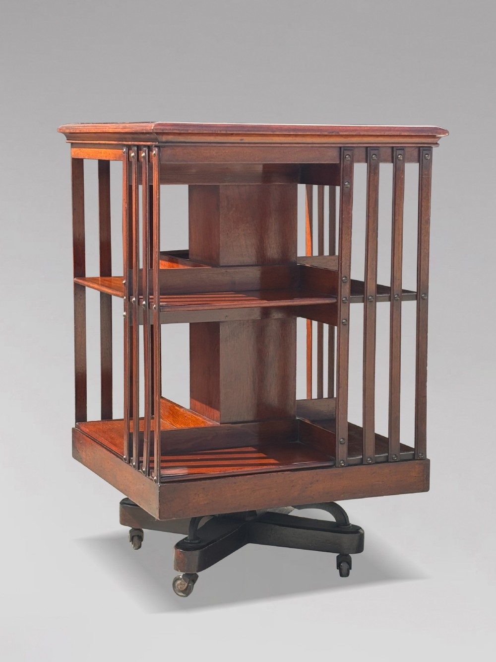 A late 19th-century Victorian mahogany revolving bookcase featuring three tiers of open shelving with vertical side slats and a square top, resting on castors. View IV