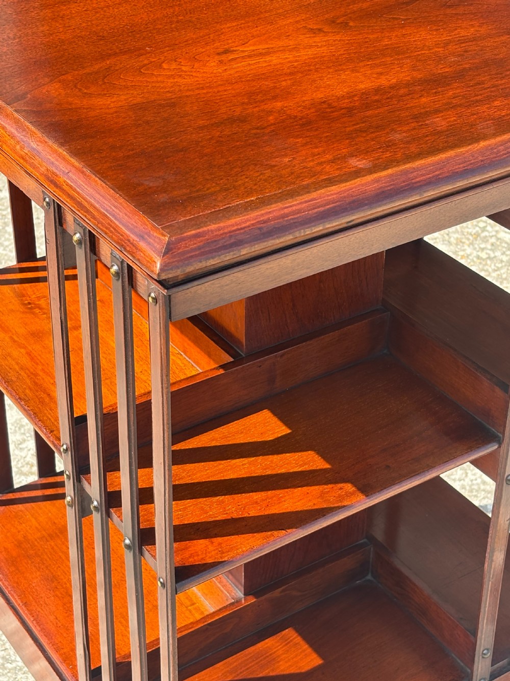 A late 19th-century Victorian mahogany revolving bookcase featuring three tiers of open shelving with vertical side slats and a square top, resting on castors. View V
