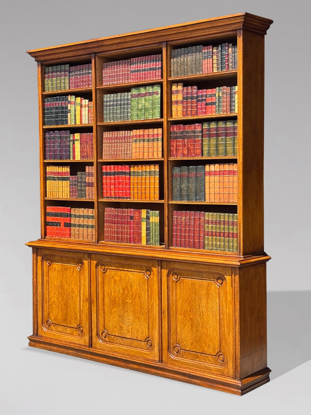 A tall 19th-century French oak open bookcase featuring a three-bay upper shelving section filled with books over a triple-door panelled cupboard base. View II