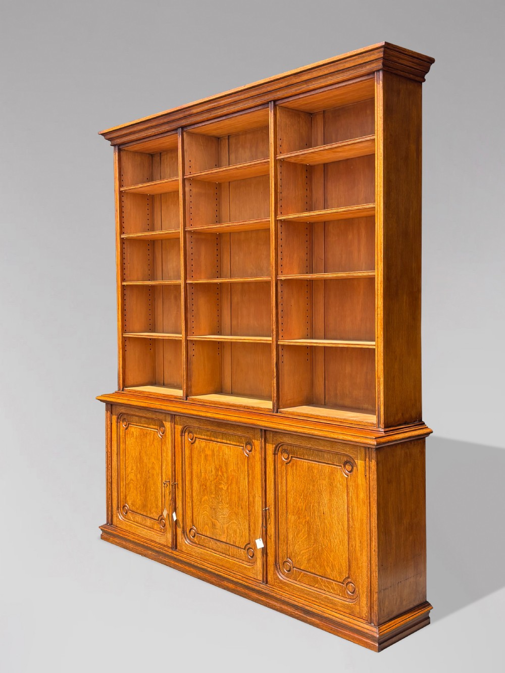 A tall 19th-century French oak open bookcase featuring a three-bay upper shelving section filled with books over a triple-door panelled cupboard base. View III