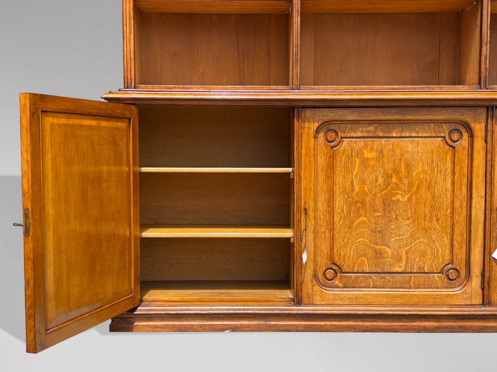 A tall 19th-century French oak open bookcase featuring a three-bay upper shelving section filled with books over a triple-door panelled cupboard base. View IV