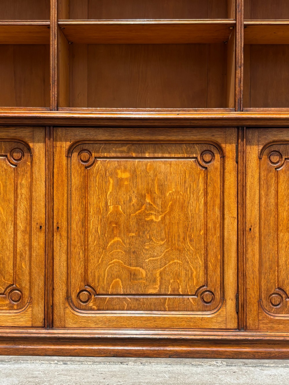 A tall 19th-century French oak open bookcase featuring a three-bay upper shelving section filled with books over a triple-door panelled cupboard base. View V