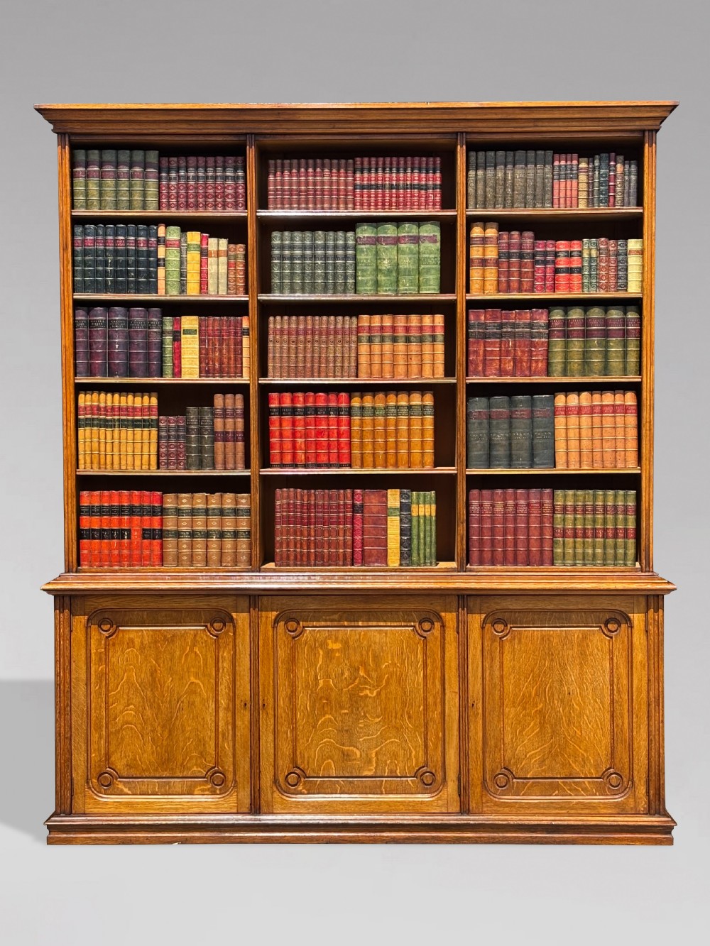 A tall 19th-century French oak open bookcase featuring a three-bay upper shelving section filled with books over a triple-door panelled cupboard base. View VII