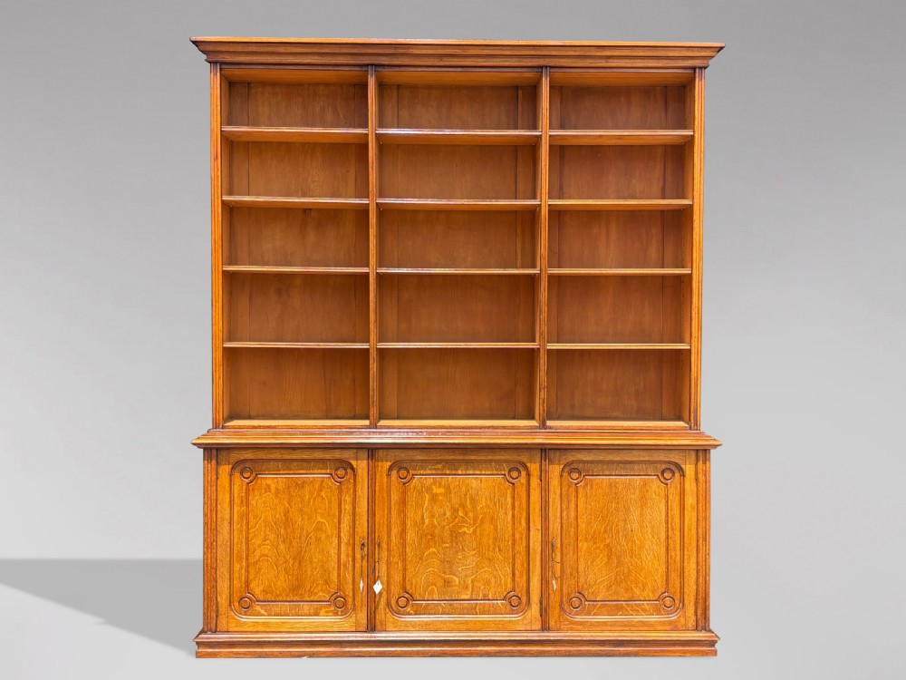A tall 19th-century French oak open bookcase featuring a three-bay upper shelving section filled with books over a triple-door panelled cupboard base. View VIII