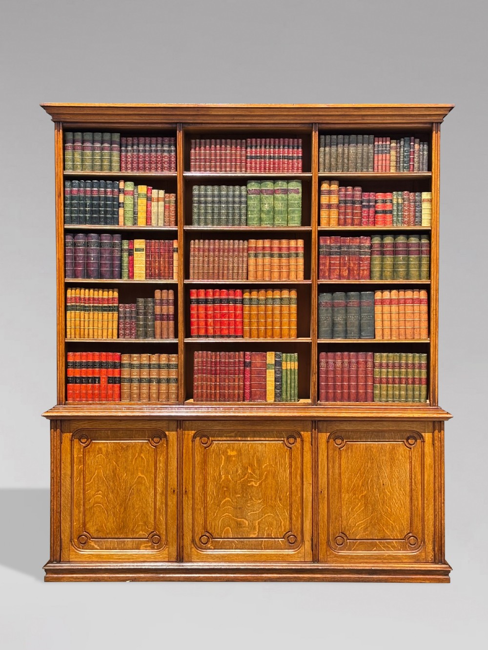 A tall 19th-century French oak open bookcase featuring a three-bay upper shelving section filled with books over a triple-door panelled cupboard base. View X