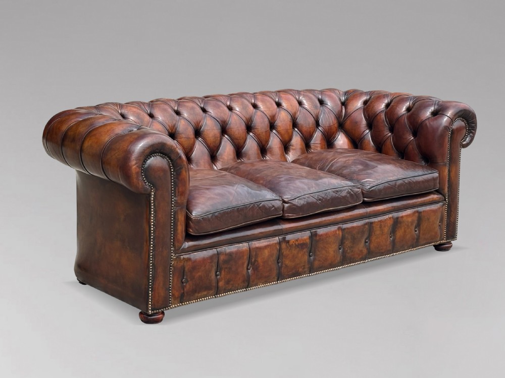 A nineteenth-century three-seater Chesterfield sofa upholstered in deep buttoned chestnut brown leather with brass stud detailing along the rolled arms.