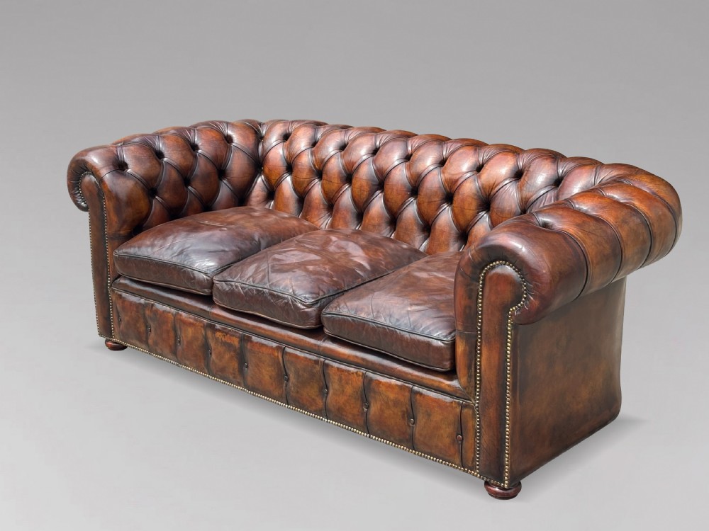 A nineteenth-century three-seater Chesterfield sofa upholstered in deep buttoned chestnut brown leather with brass stud detailing along the rolled arms. View II