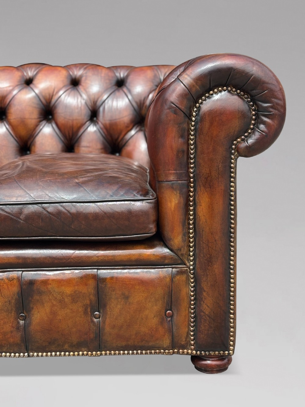 A nineteenth-century three-seater Chesterfield sofa upholstered in deep buttoned chestnut brown leather with brass stud detailing along the rolled arms. View V