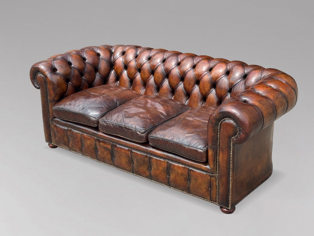 A nineteenth-century three-seater Chesterfield sofa upholstered in deep buttoned chestnut brown leather with brass stud detailing along the rolled arms. View VI