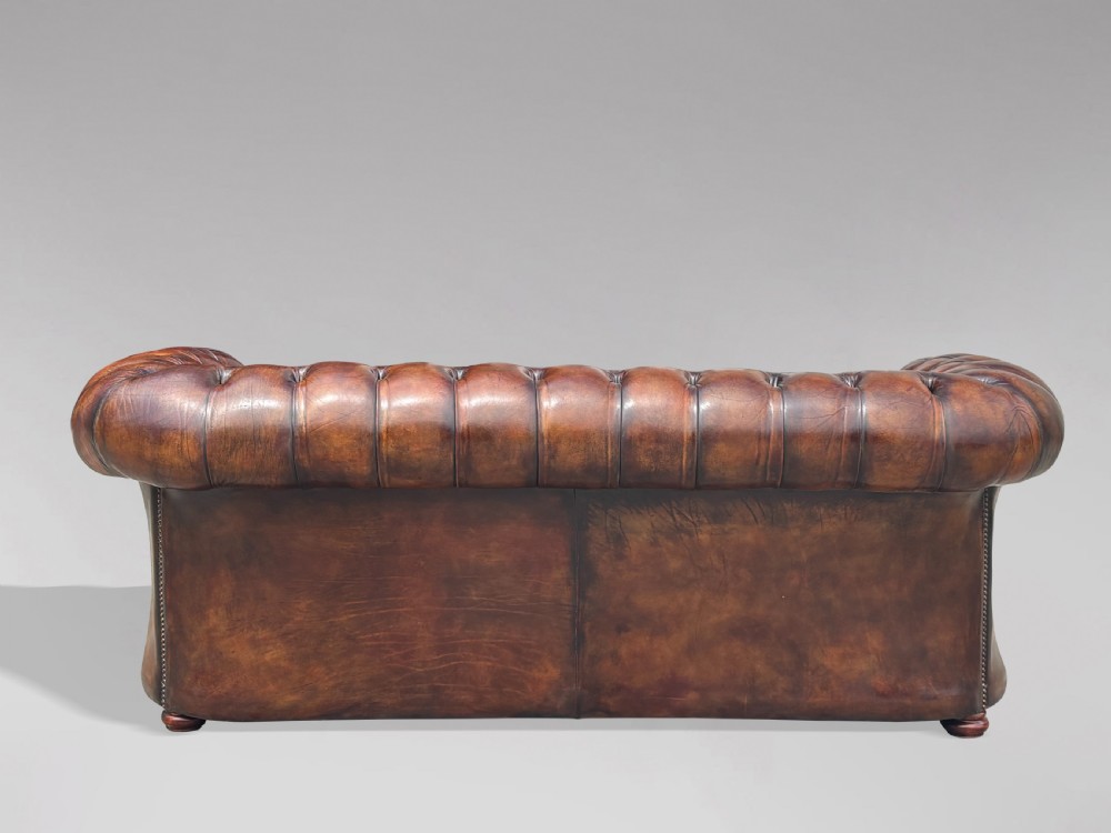 A nineteenth-century three-seater Chesterfield sofa upholstered in deep buttoned chestnut brown leather with brass stud detailing along the rolled arms. View VII