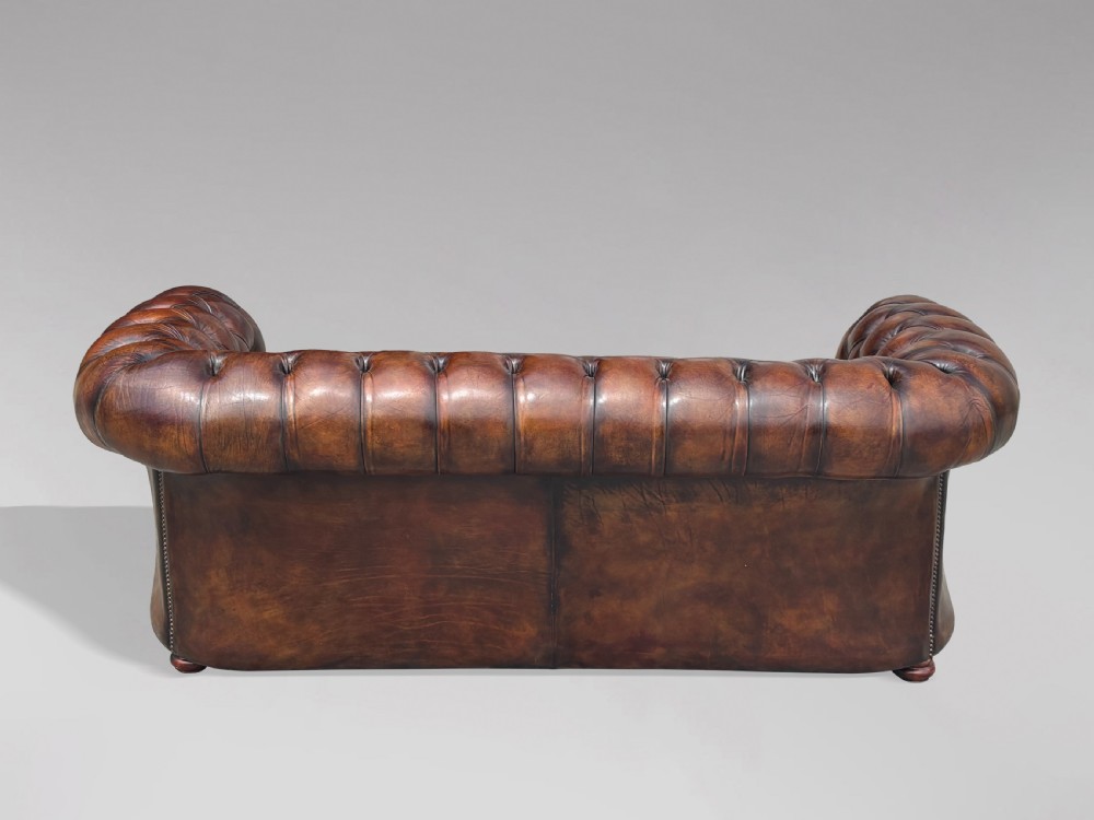 A nineteenth-century three-seater Chesterfield sofa upholstered in deep buttoned chestnut brown leather with brass stud detailing along the rolled arms. View VIII