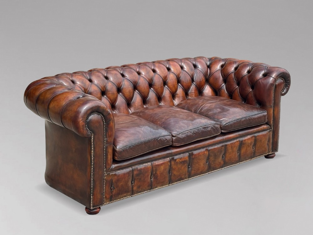 A nineteenth-century three-seater Chesterfield sofa upholstered in deep buttoned chestnut brown leather with brass stud detailing along the rolled arms. View IX