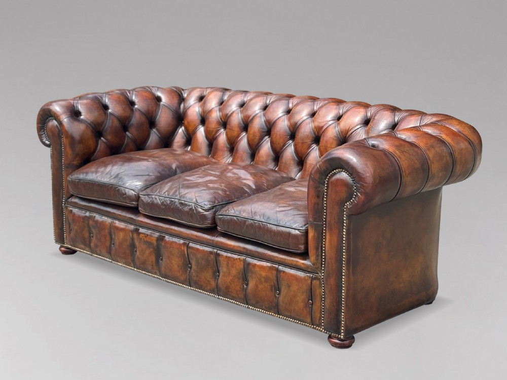 A nineteenth-century three-seater Chesterfield sofa upholstered in deep buttoned chestnut brown leather with brass stud detailing along the rolled arms. View XI