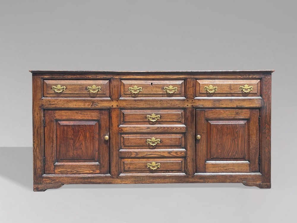 An 18th-century George II solid oak dresser base featuring multiple drawers, panelled cupboard doors, and brass drop handles. View II