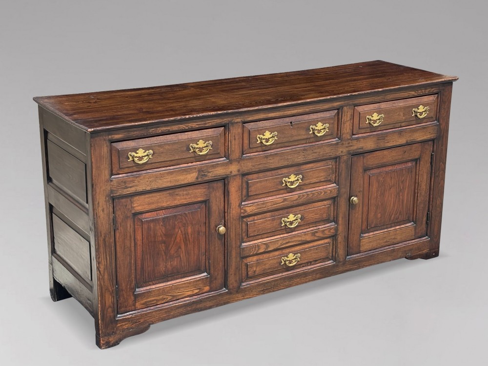 An 18th-century George II solid oak dresser base featuring multiple drawers, panelled cupboard doors, and brass drop handles. View IV