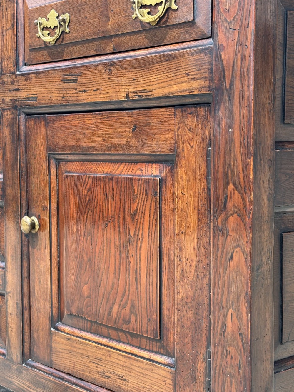 An 18th-century George II solid oak dresser base featuring multiple drawers, panelled cupboard doors, and brass drop handles. View VIII