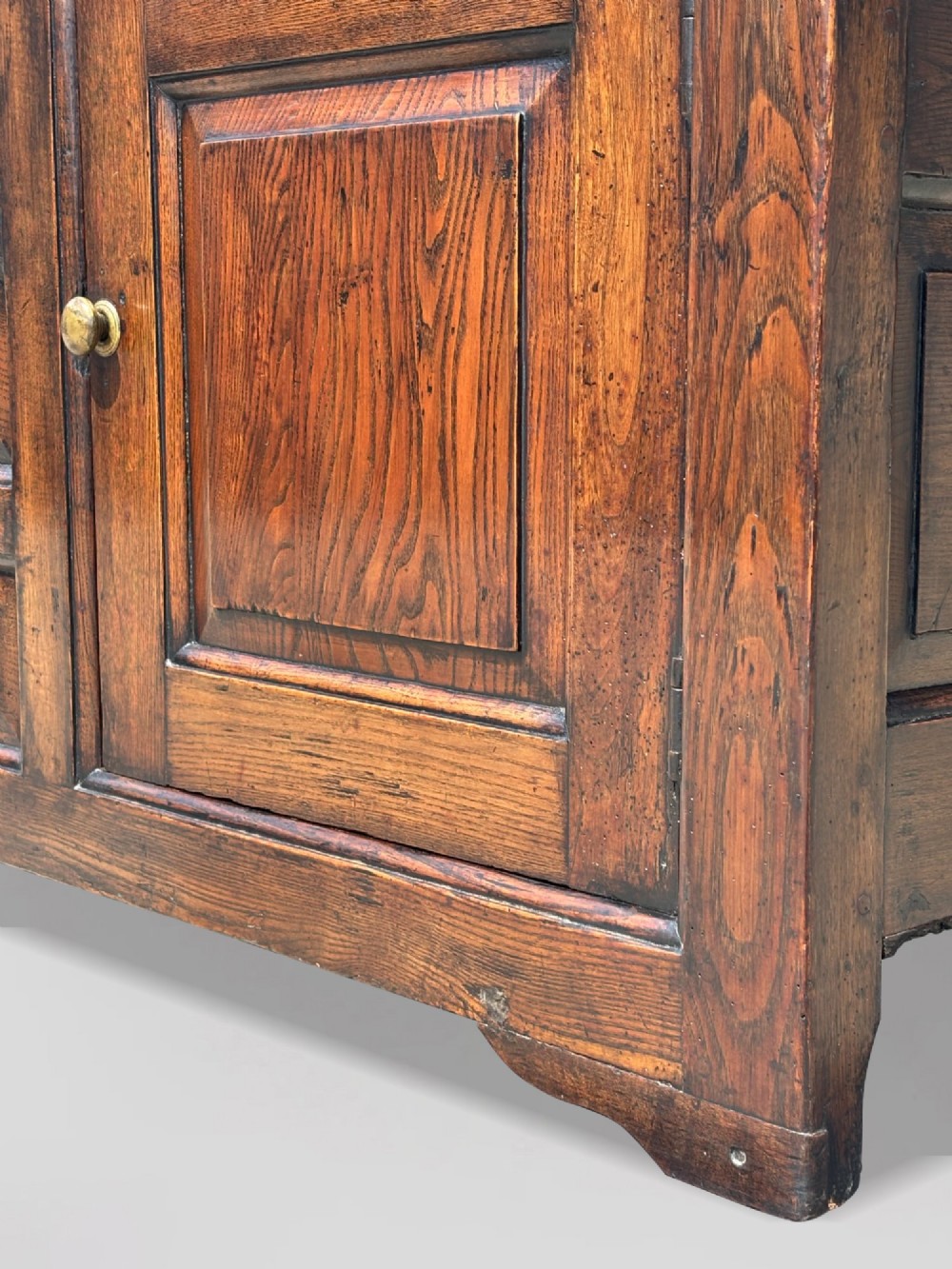 An 18th-century George II solid oak dresser base featuring multiple drawers, panelled cupboard doors, and brass drop handles. View X