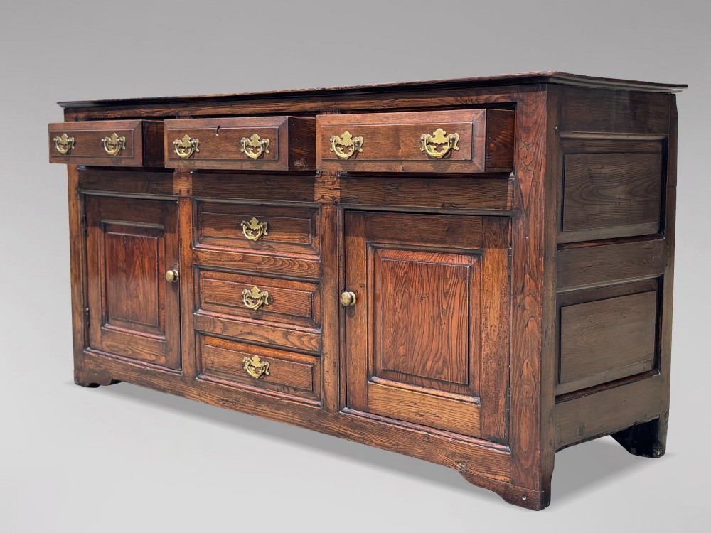 An 18th-century George II solid oak dresser base featuring multiple drawers, panelled cupboard doors, and brass drop handles. View XI