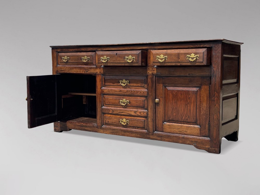 An 18th-century George II solid oak dresser base featuring multiple drawers, panelled cupboard doors, and brass drop handles. View XIII