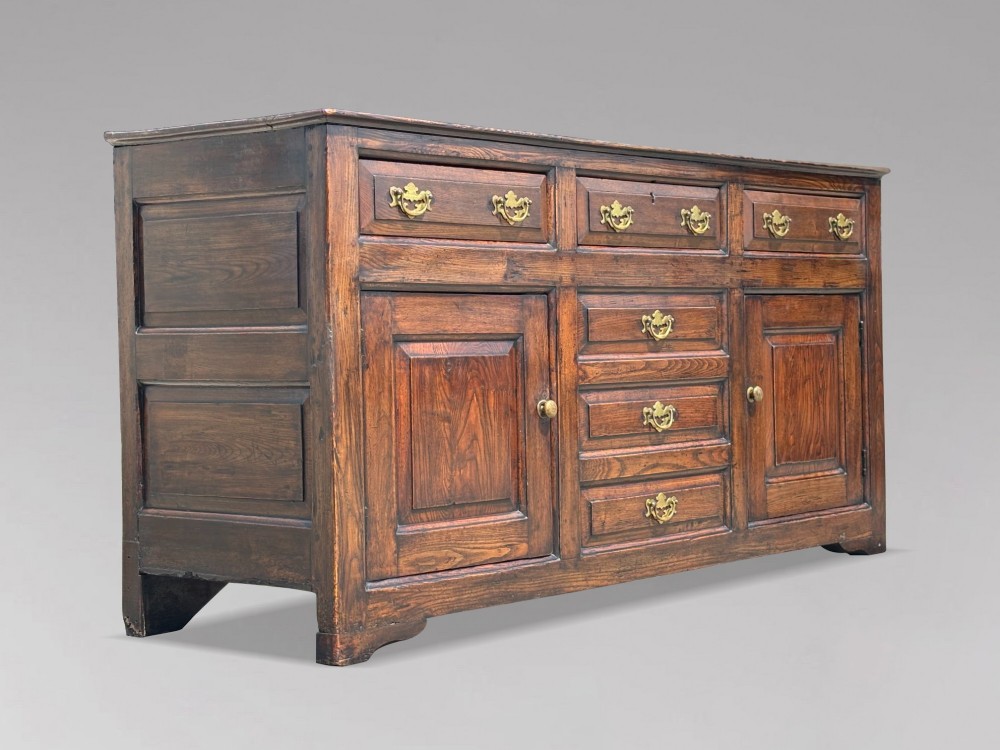 An 18th-century George II solid oak dresser base featuring multiple drawers, panelled cupboard doors, and brass drop handles. View XIV
