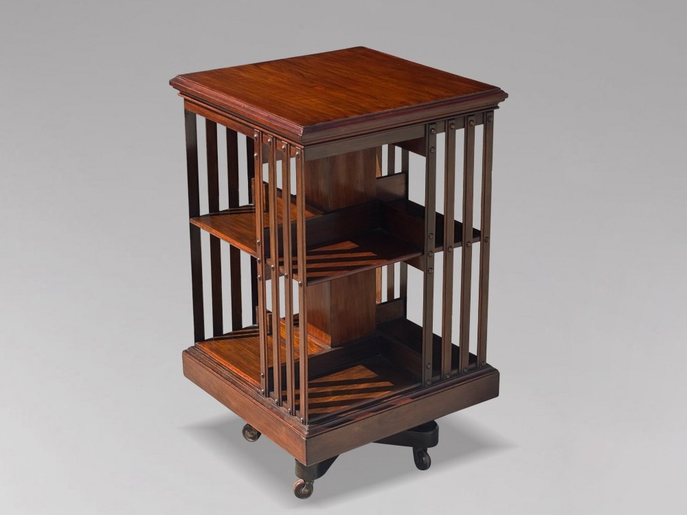 A 19th-century Victorian dark mahogany revolving bookcase featuring two slatted tiers on a central rotating base with castors.