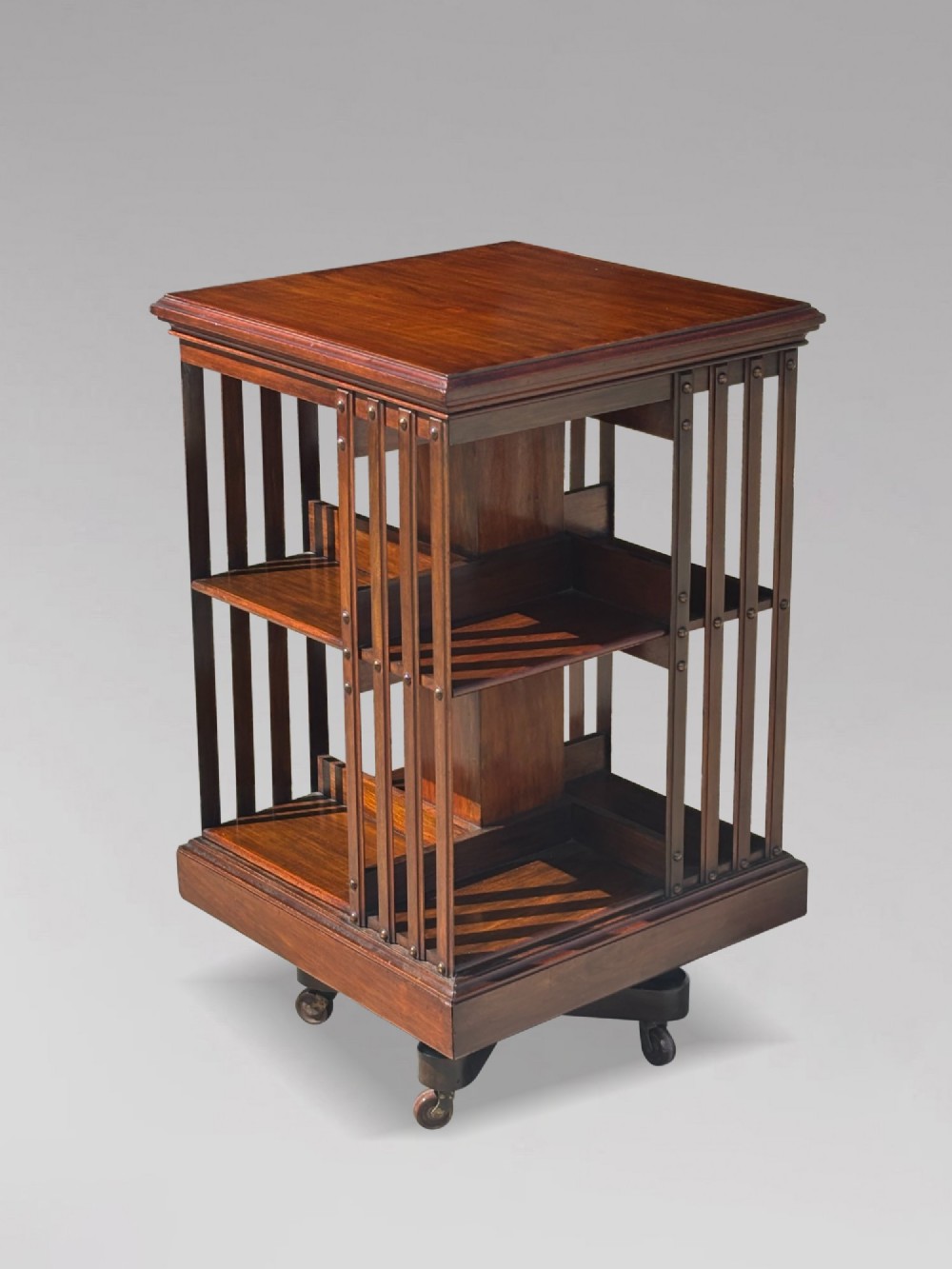 A 19th-century Victorian dark mahogany revolving bookcase featuring two slatted tiers on a central rotating base with castors. View II