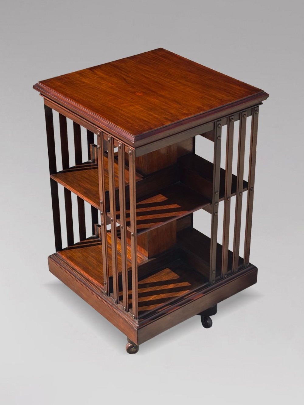 A 19th-century Victorian dark mahogany revolving bookcase featuring two slatted tiers on a central rotating base with castors. View III