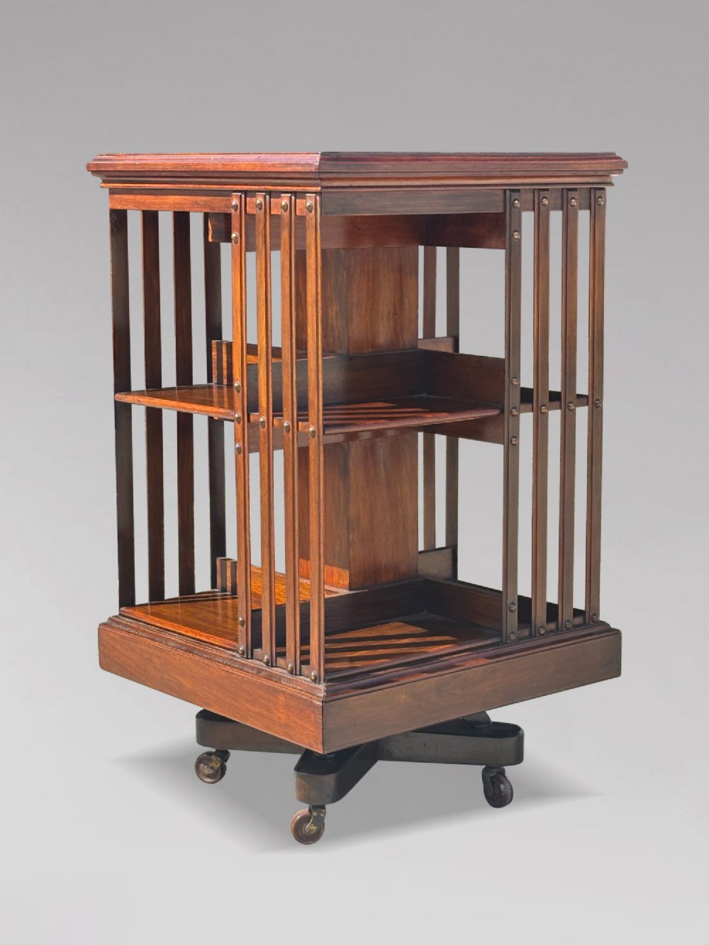 A 19th-century Victorian dark mahogany revolving bookcase featuring two slatted tiers on a central rotating base with castors. View V