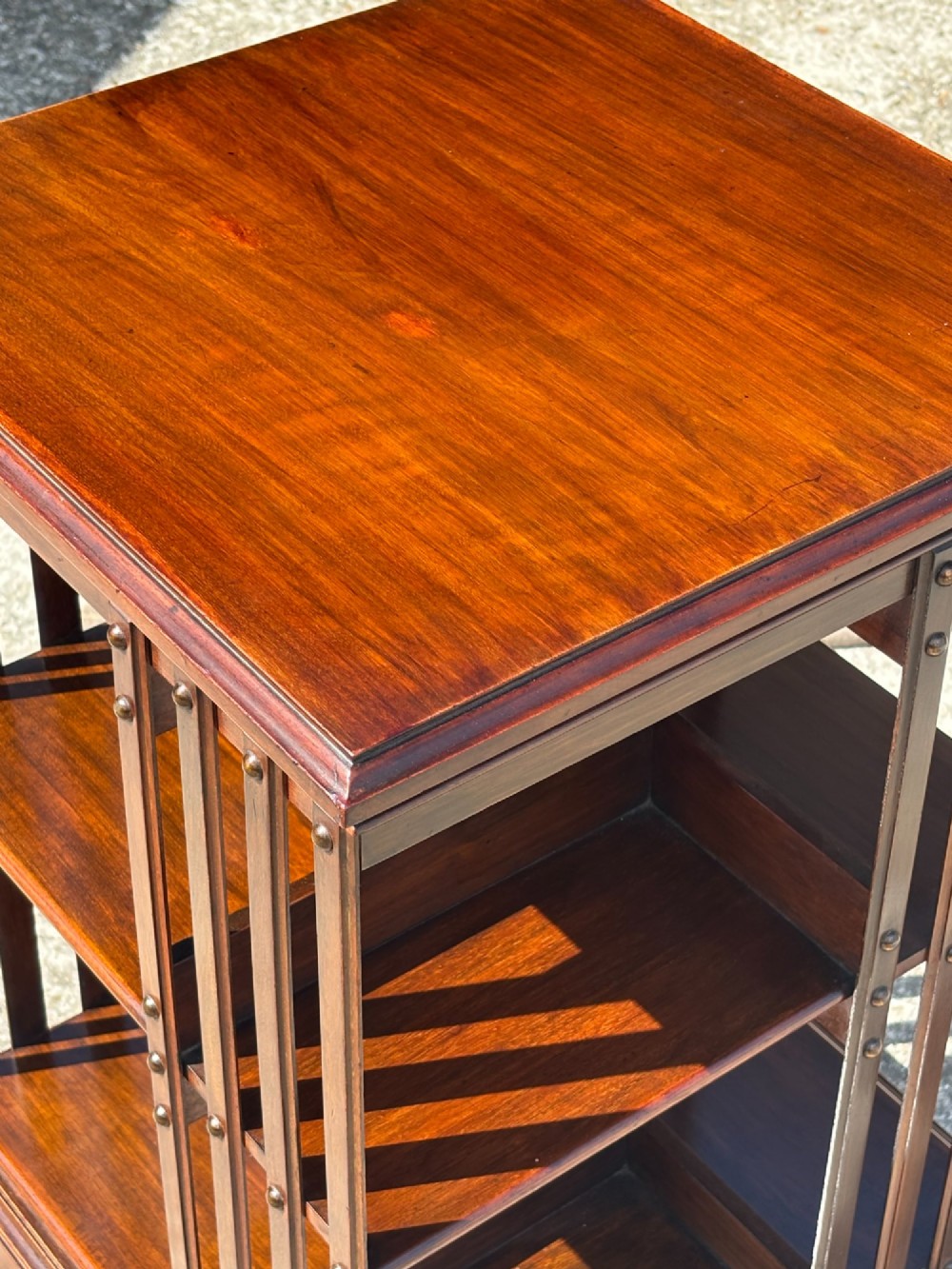 A 19th-century Victorian dark mahogany revolving bookcase featuring two slatted tiers on a central rotating base with castors. View VII