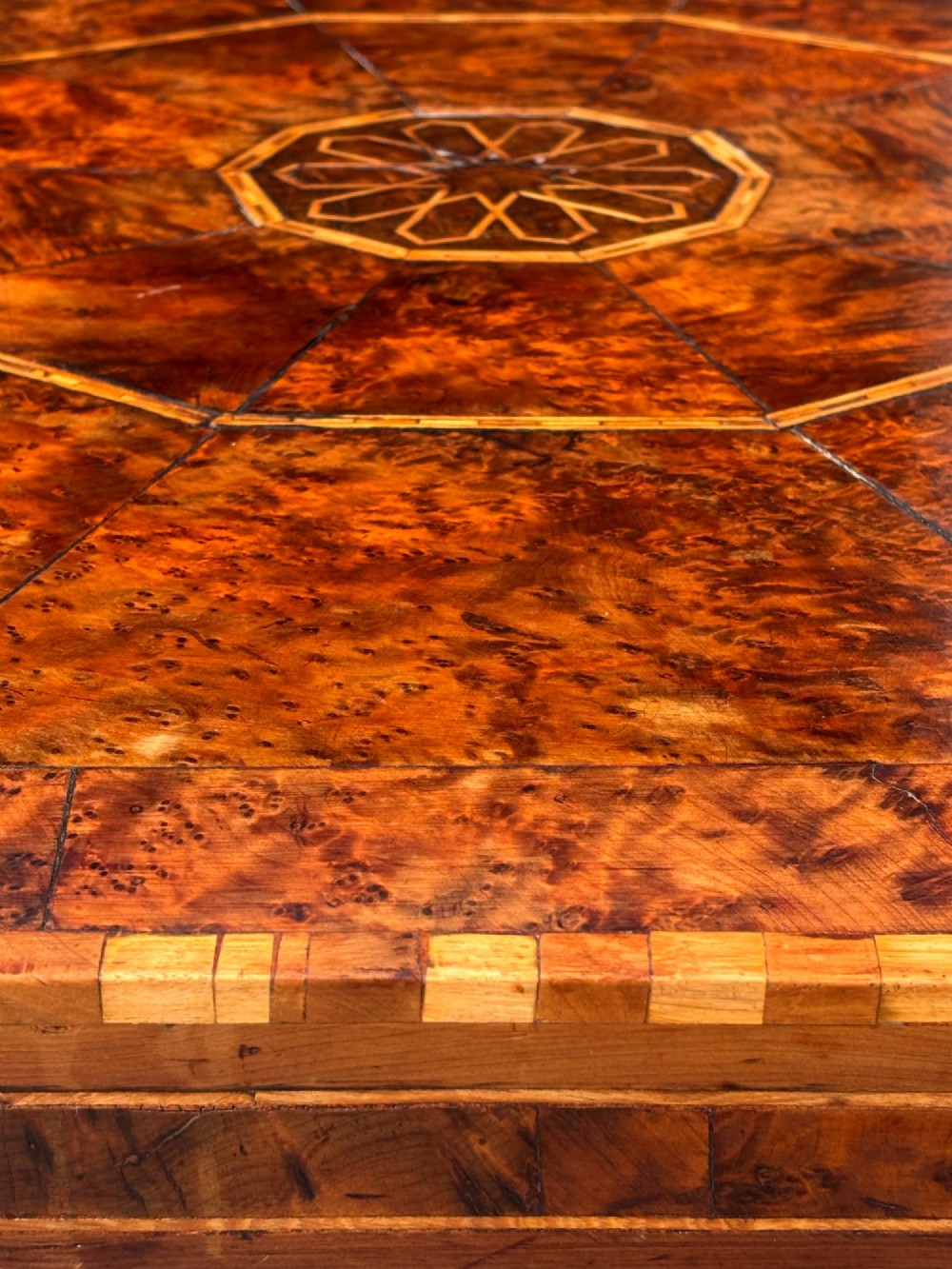 An octagonal 19th-century burr yew wood coffee table featuring radiating veneer panels, a central inlaid star motif, and a checkered border. View V
