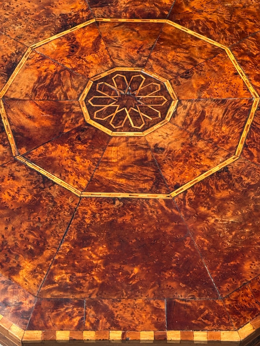 An octagonal 19th-century burr yew wood coffee table featuring radiating veneer panels, a central inlaid star motif, and a checkered border. View VIII
