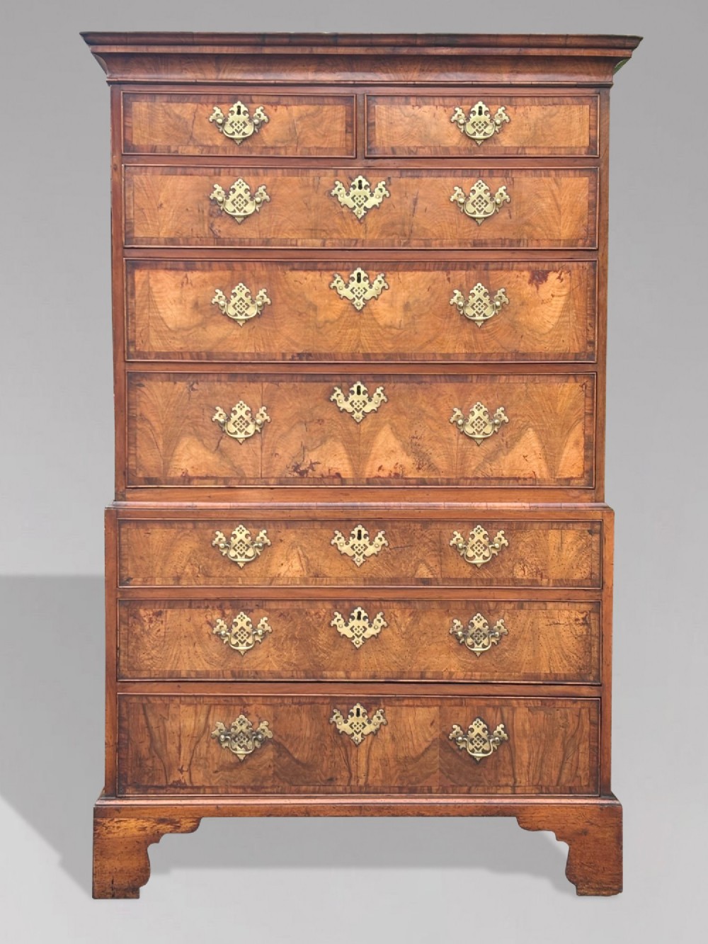 An eighteenth-century George II walnut chest on chest featuring two short over six long graduated drawers with decorative brass handles, keyhole escutcheons, and bracket feet.