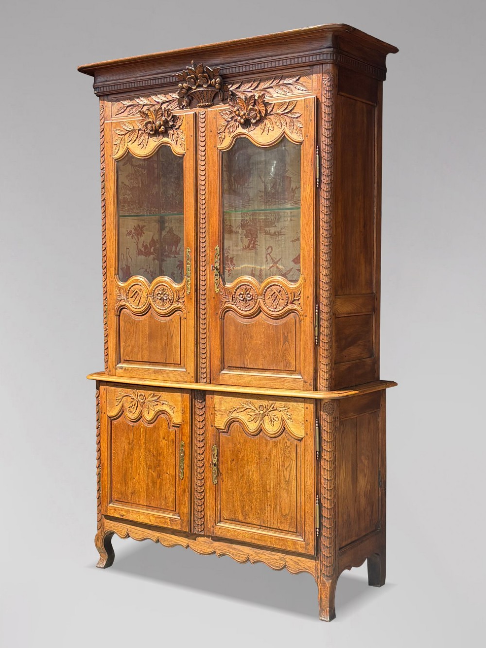 An 18th-century carved oak French buffet deux corps featuring upper glazed doors lined with fabric above a panelled lower cabinet with relief carvings. View II