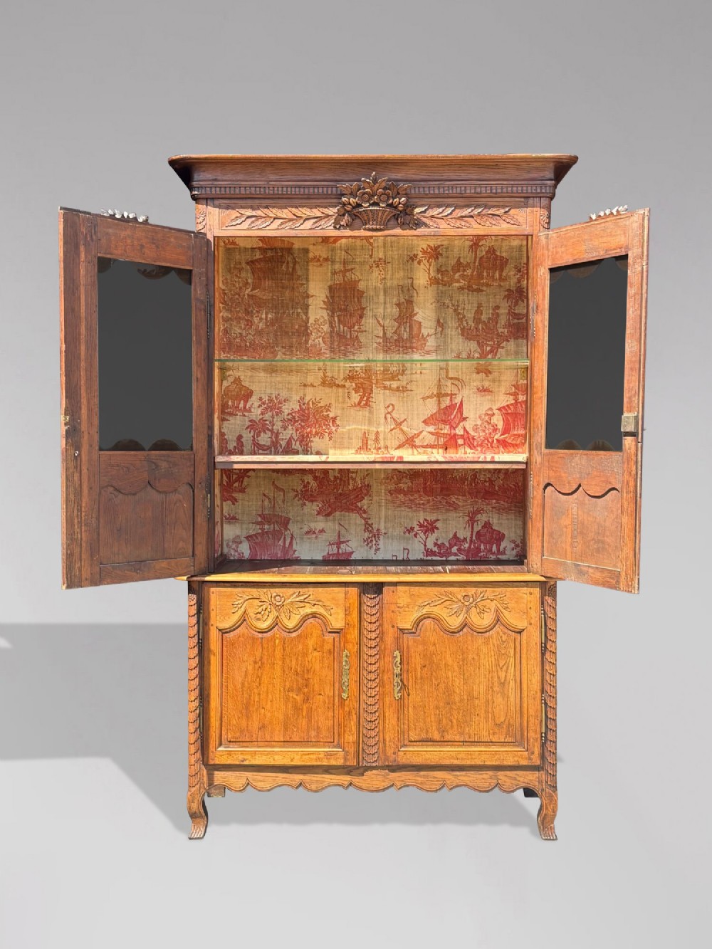 An 18th-century carved oak French buffet deux corps featuring upper glazed doors lined with fabric above a panelled lower cabinet with relief carvings. View III