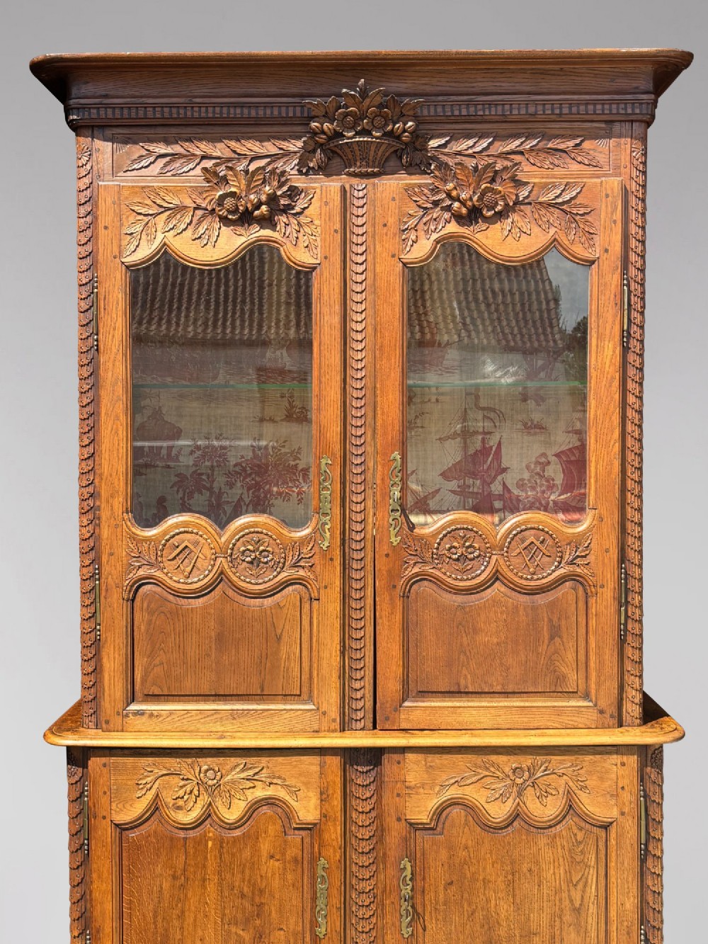 An 18th-century carved oak French buffet deux corps featuring upper glazed doors lined with fabric above a panelled lower cabinet with relief carvings. View IV