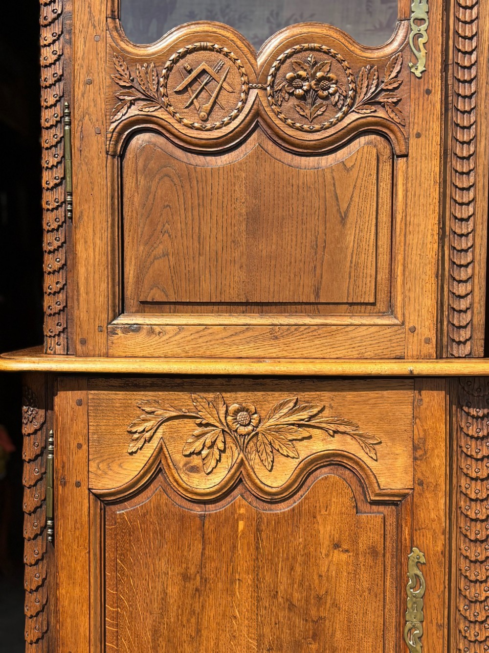 An 18th-century carved oak French buffet deux corps featuring upper glazed doors lined with fabric above a panelled lower cabinet with relief carvings. View X