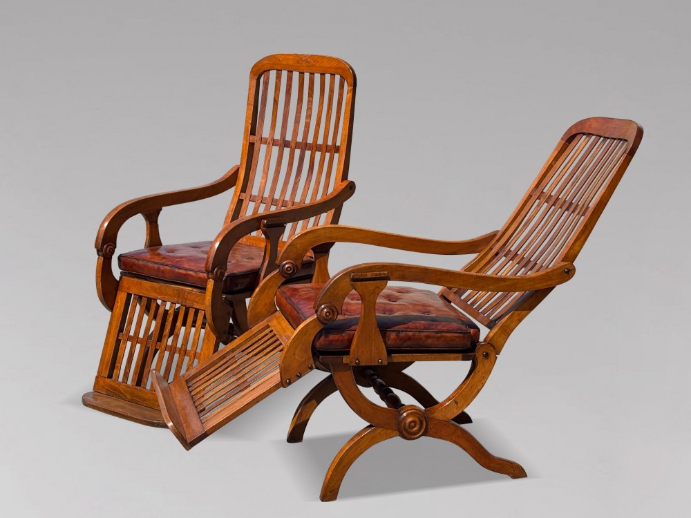 A pair of 19th-century Victorian walnut reclining armchairs featuring slatted backrests, extendable footrests, curved X-frame bases, and brown leather seat cushions. View II