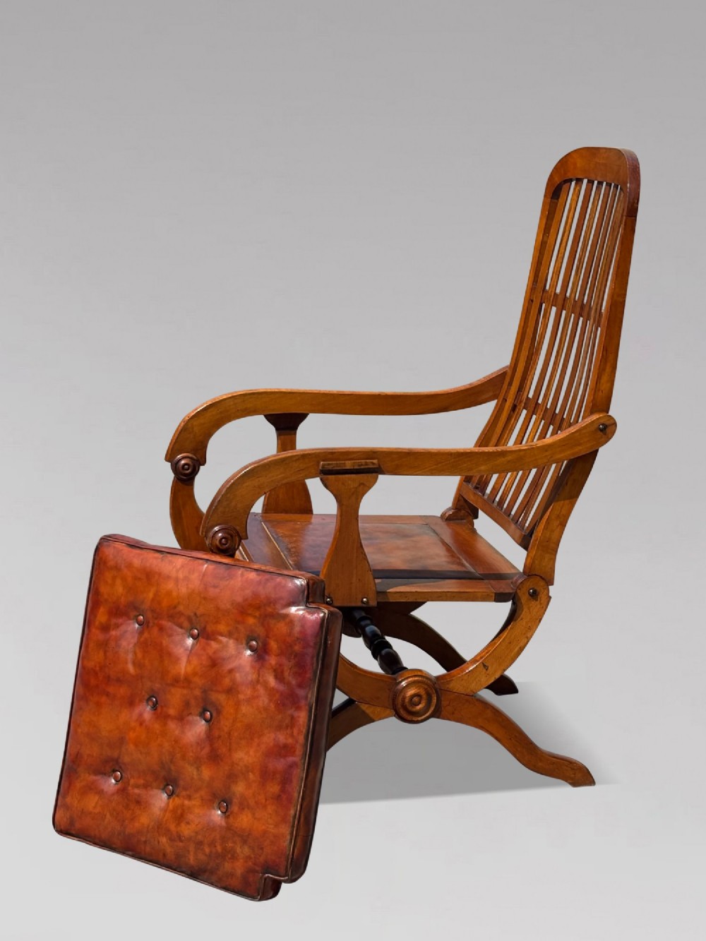 A pair of 19th-century Victorian walnut reclining armchairs featuring slatted backrests, extendable footrests, curved X-frame bases, and brown leather seat cushions. View IV