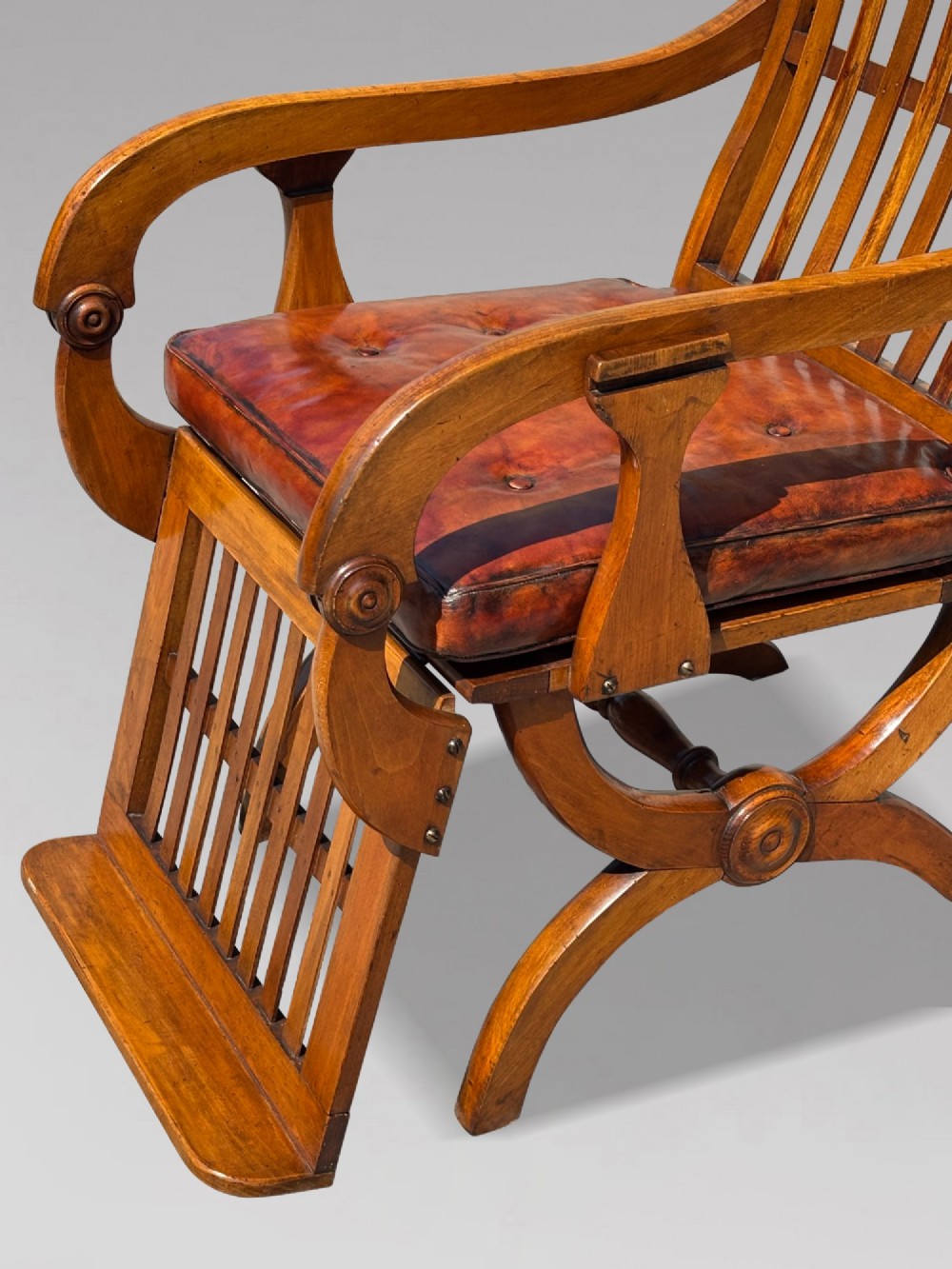 A pair of 19th-century Victorian walnut reclining armchairs featuring slatted backrests, extendable footrests, curved X-frame bases, and brown leather seat cushions. View V