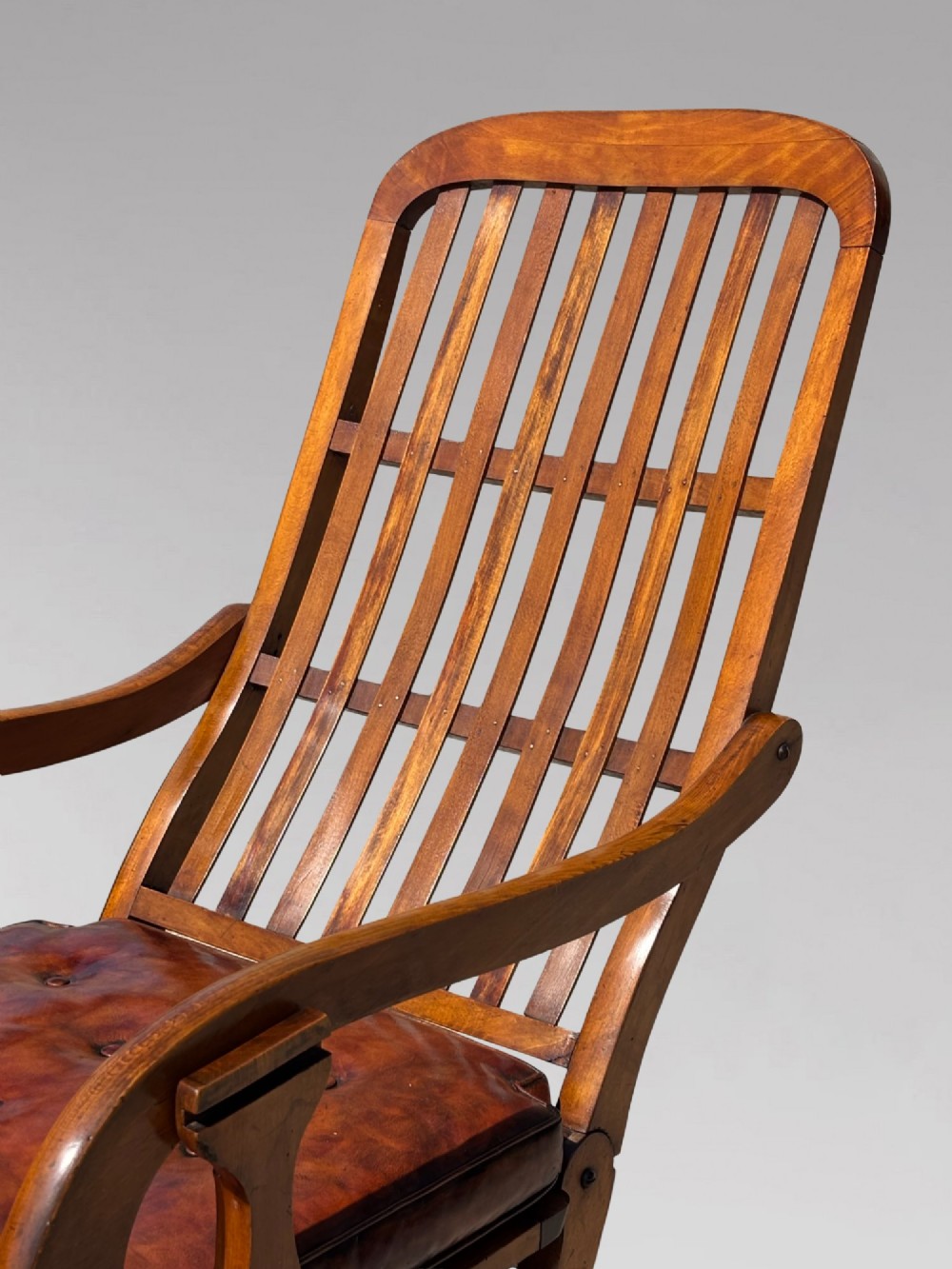 A pair of 19th-century Victorian walnut reclining armchairs featuring slatted backrests, extendable footrests, curved X-frame bases, and brown leather seat cushions. View VI