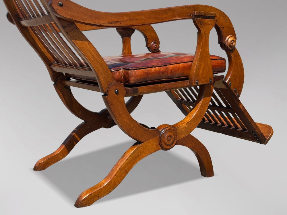 A pair of 19th-century Victorian walnut reclining armchairs featuring slatted backrests, extendable footrests, curved X-frame bases, and brown leather seat cushions. View VII