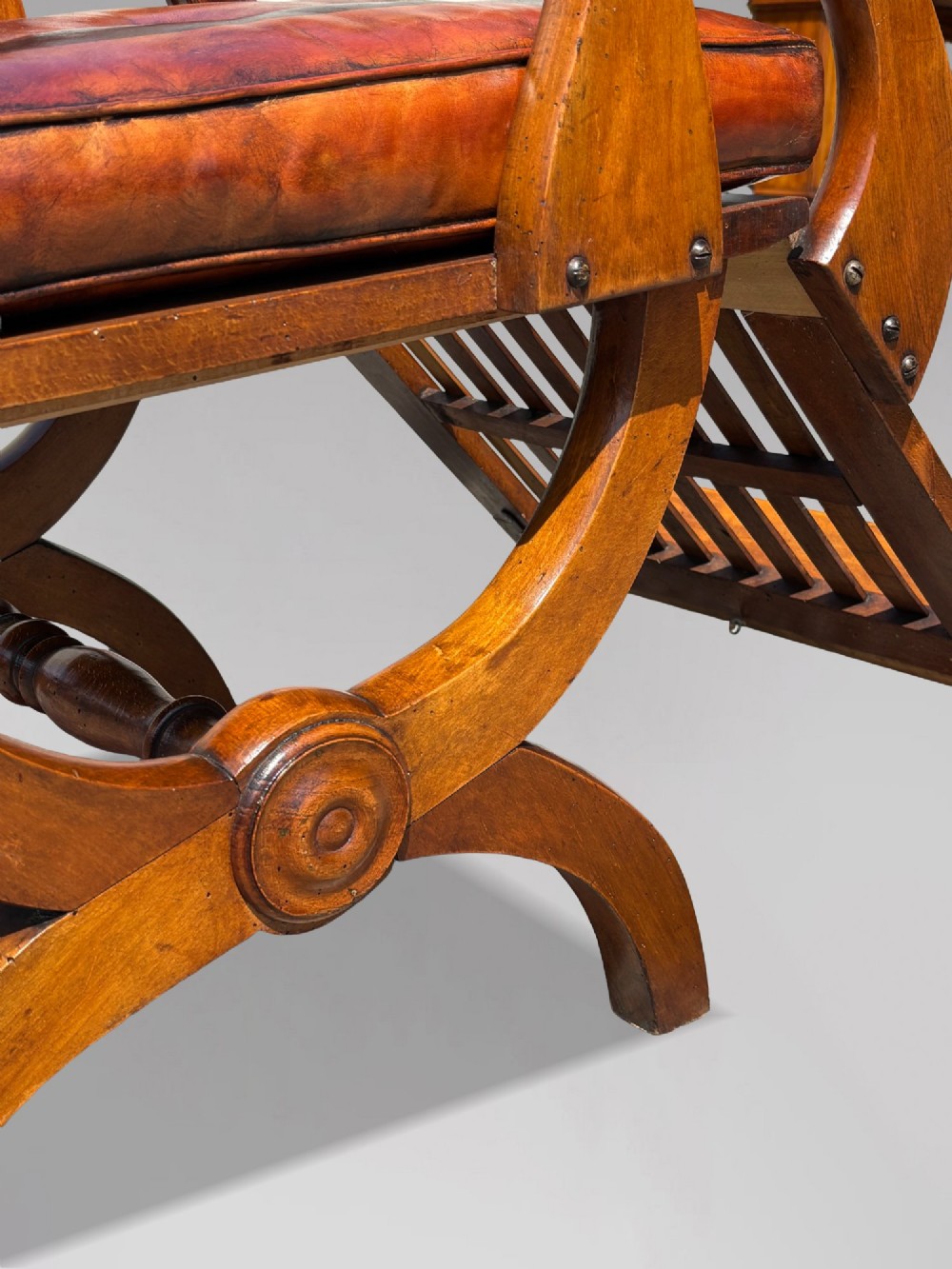 A pair of 19th-century Victorian walnut reclining armchairs featuring slatted backrests, extendable footrests, curved X-frame bases, and brown leather seat cushions. View IX