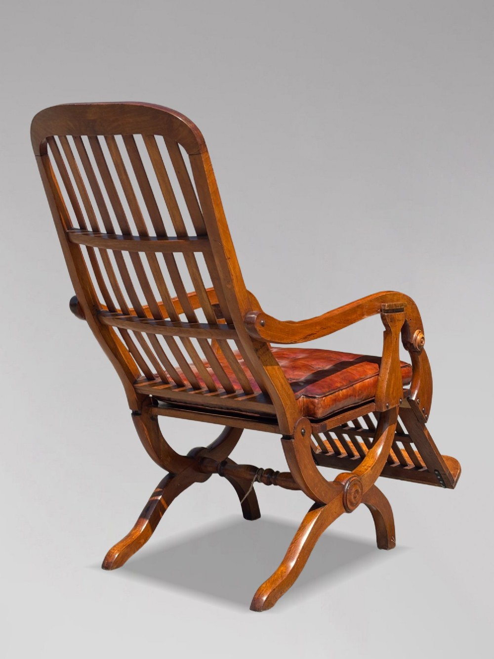 A pair of 19th-century Victorian walnut reclining armchairs featuring slatted backrests, extendable footrests, curved X-frame bases, and brown leather seat cushions. View X